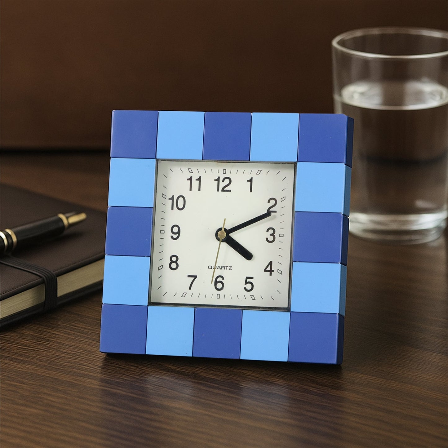 Modern square table clock with a bold frame, displayed on a desk.