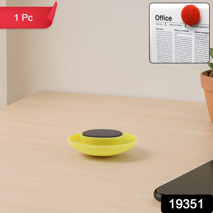 Hand holding yellow circular magnet securing paper on board